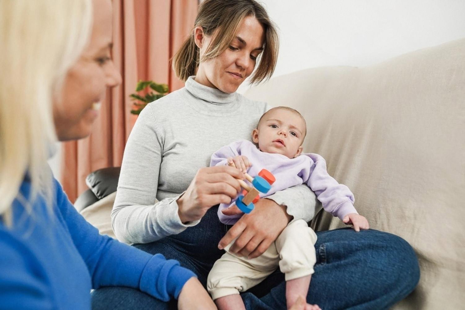 Mother holding a baby who is grasping a colourful wooden tactile rattle
