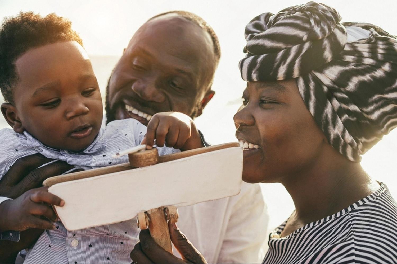 Parents smiling as their baby explores a wooden airplane toy with different textures
